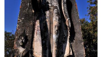A large Buddha statue with a smaller statue beside it, both set against a clear blue sky.