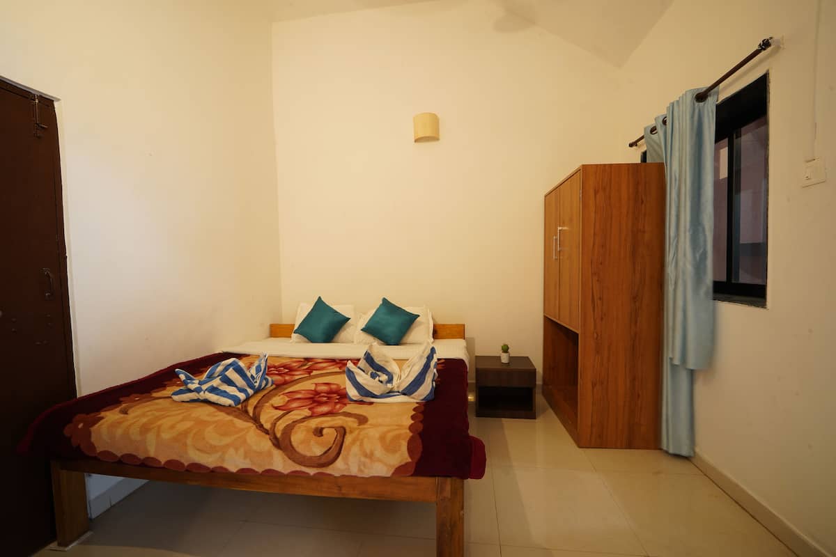 A bedroom with a bed, pillows, a nightstand, a wardrobe, and a window with curtains.