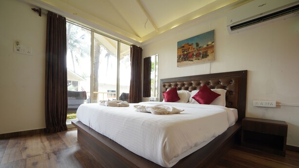 Una cama grande con cabecera de madera, ropa de cama blanca y almohadas rojas y blancas. Hay una mesita de noche y un enchufe en la pared.