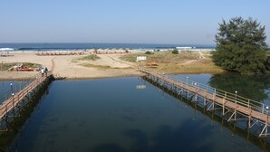 Una playa con un muelle de madera que se adentra en aguas tranquilas, arena dorada y un cielo despejado.