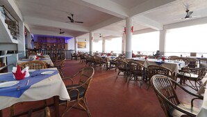 Un restaurante espacioso con techos altos, varias mesas y sillas, y amplios ventanales.