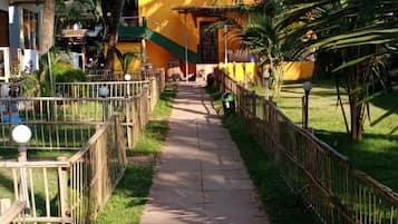 A pathway leading to a building with a yellow facade, surrounded by palm trees and a fenced area.