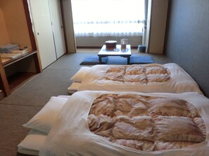 Habitación de hotel con dos camas, una mesita con tetera y tazas, y vista al exterior a través de una ventana.