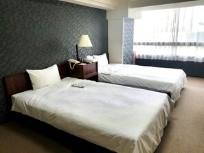 Habitación de hotel con dos camas, una mesita de noche con lámpara y una ventana con cortinas.
