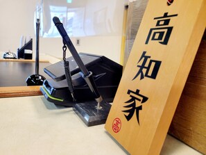 Un letrero de madera con caracteres japoneses, un dispositivo electrónico negro y una lámpara sobre una mesa.