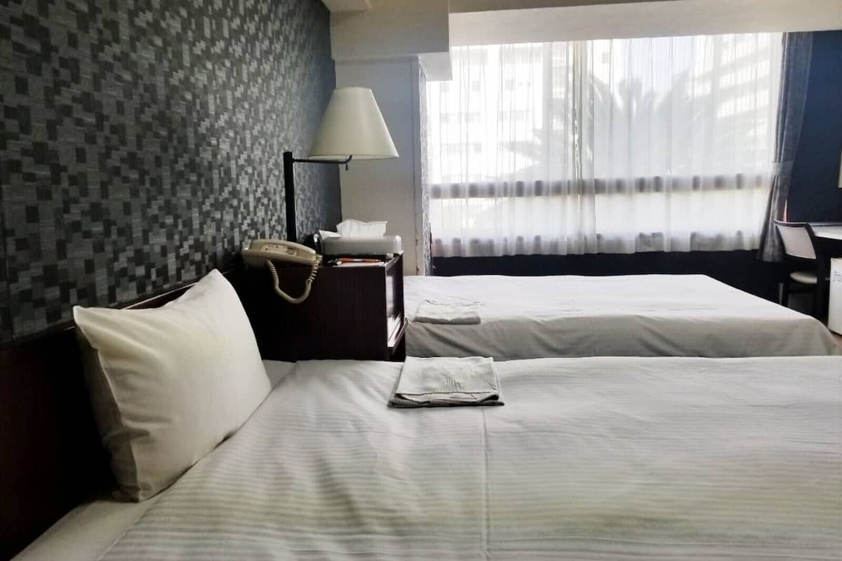 A hotel room with two beds, a desk, a lamp, and a telephone.