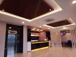 A modern hotel reception area with a digital elevator display, a reception desk, and a television screen.
