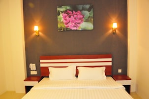 A hotel room with a bed, two bedside tables, a wall-mounted lamp, and a framed picture of flowers.