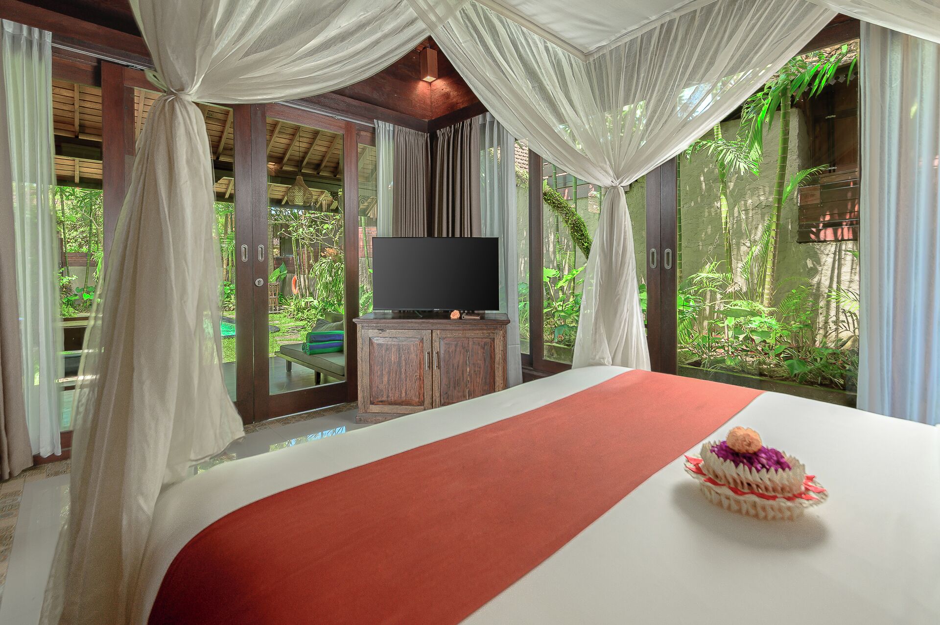 A bedroom with a bed, a television, and a view of greenery.