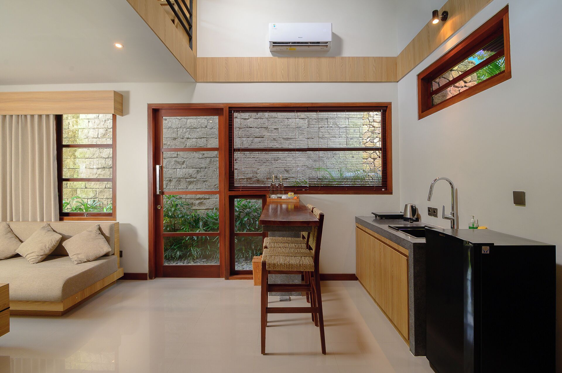 A modern kitchen with a built-in stove, a dining area with a wooden table and chairs, and a large window with a view of greenery.