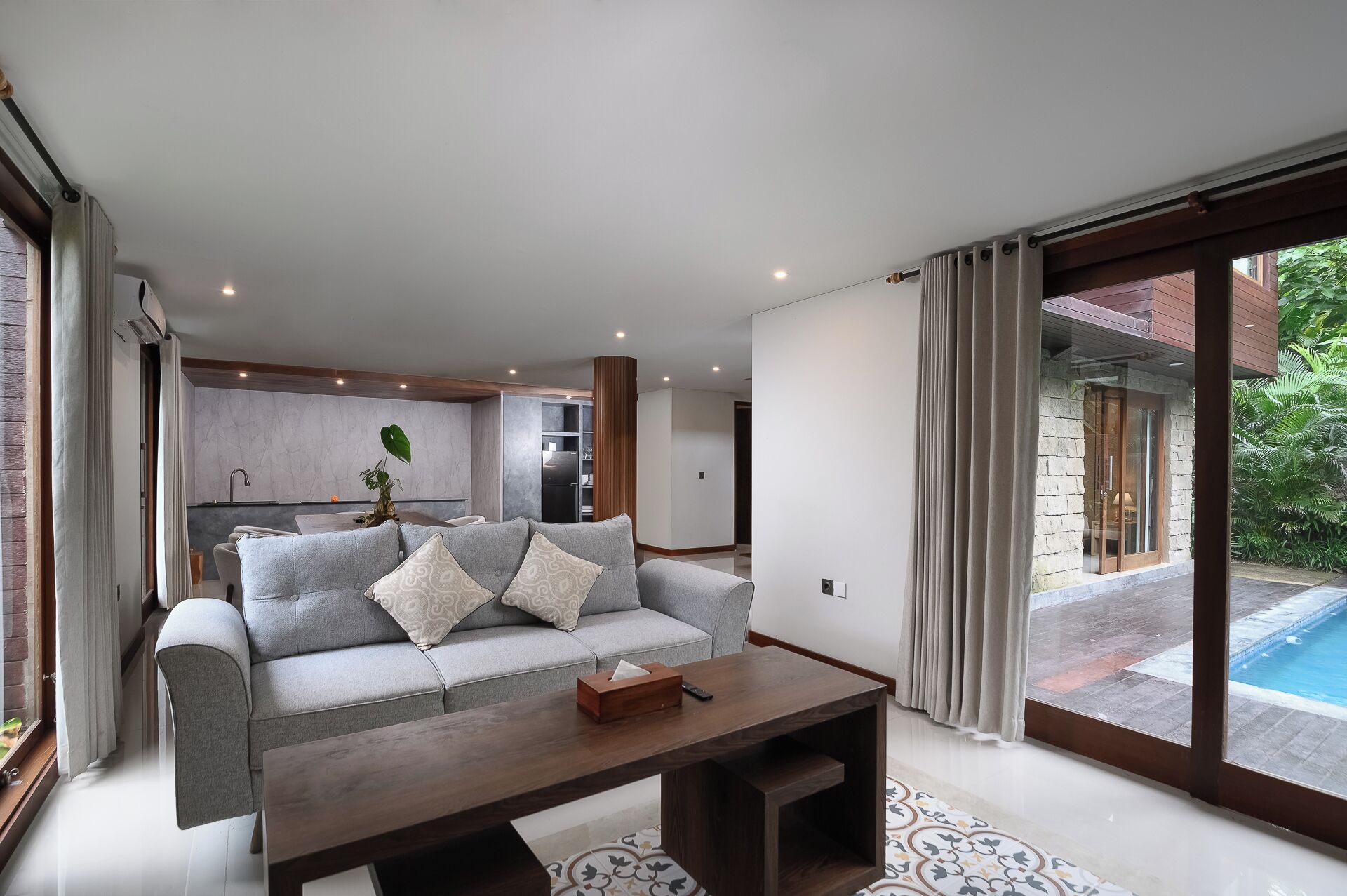 Un salon moderne avec un canapé gris, une table basse en bois et une vue sur une piscine.