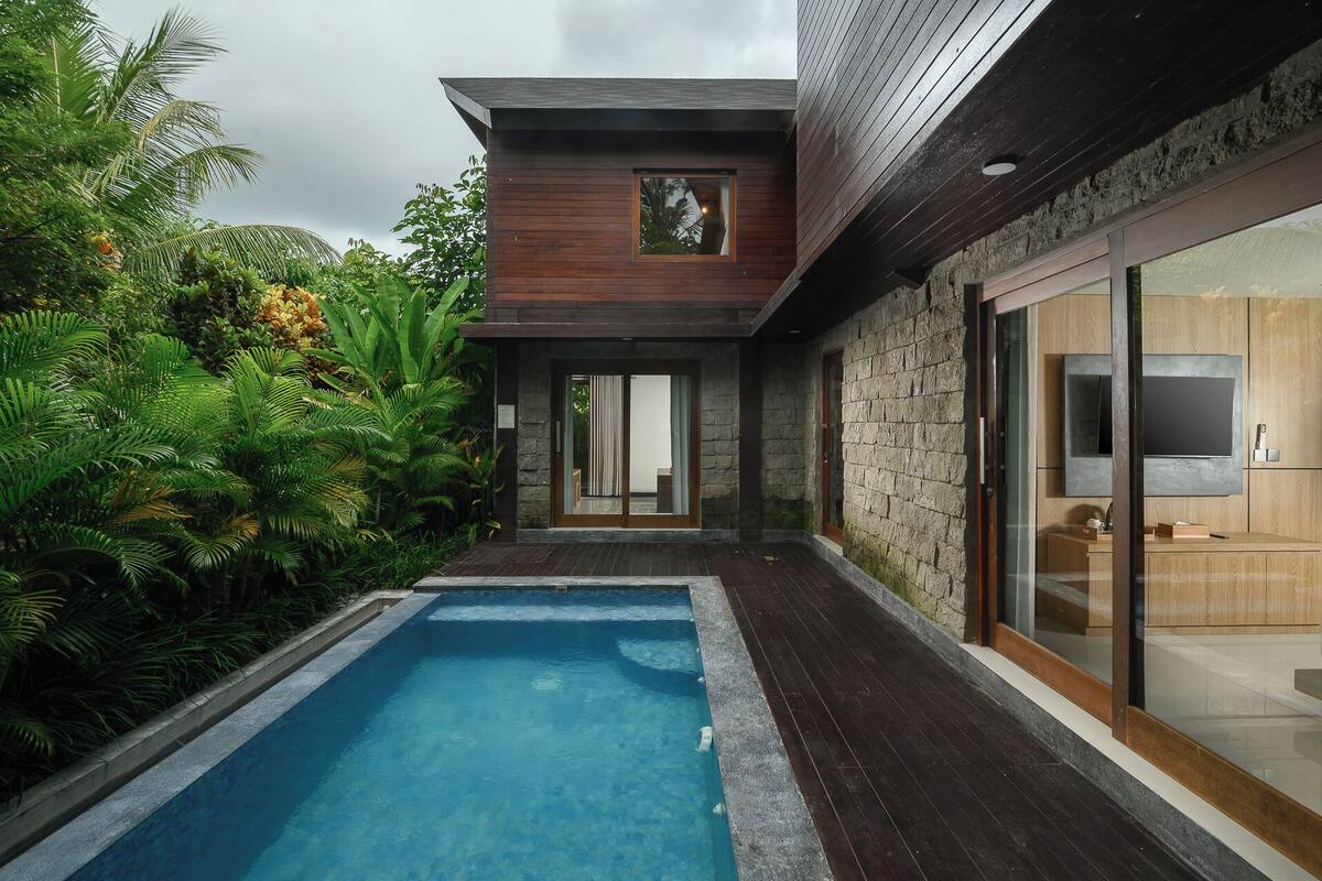 A modern house with a swimming pool, stone walls, and a large glass door leading to a living area.