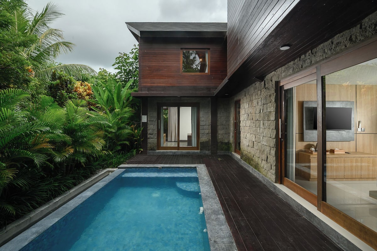 Uma casa moderna com piscina, paredes de pedra e uma grande porta de vidro que dá para uma sala de estar.