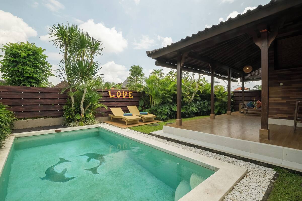 A swimming pool with lounge chairs, a wooden deck, and a covered seating area.