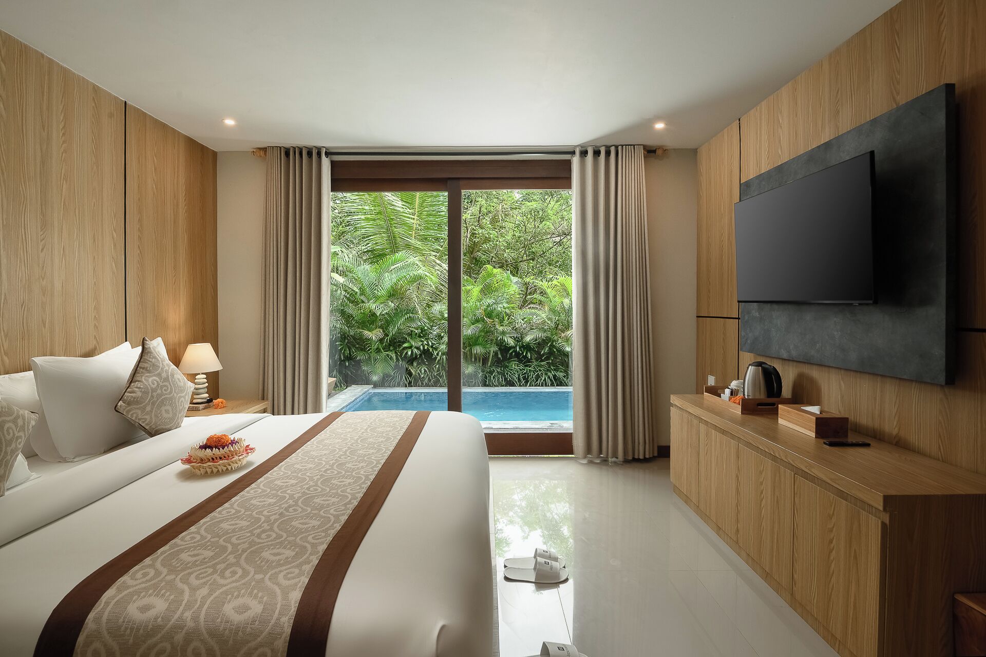 A modern hotel room with a large bed, a TV, a pool view, and a wooden cabinet.