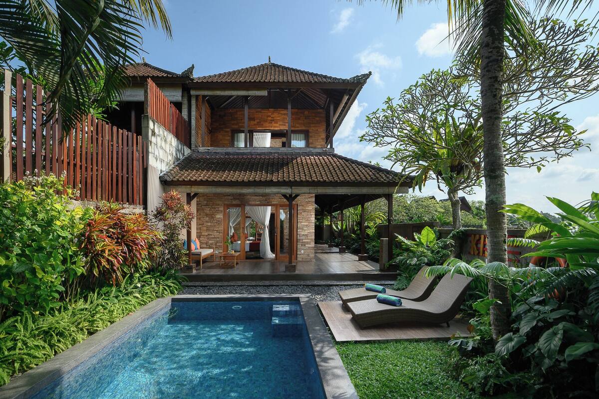 A two-story house with a swimming pool, outdoor seating, and lush greenery.