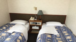 A hotel room with two beds, each with a patterned bedspread, a bedside table with a lamp, a phone, and a small shelf with a tissue box. - Hotel Town Nishikigawa (Kochi)