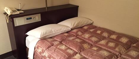 A hotel room with a bed, a bedside table with a lamp, a phone, and a digital clock.