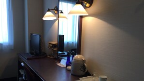 A hotel room with a desk, a computer, a coffee maker, a cup, and a remote control.