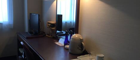 Una habitación de hotel con escritorio, computadora, cafetera, taza y control remoto.