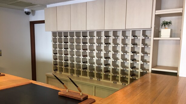 A room with a wooden floor, a black table, and a wall of numbered shoe racks. - Hotel Town Nishikigawa (Kochi)