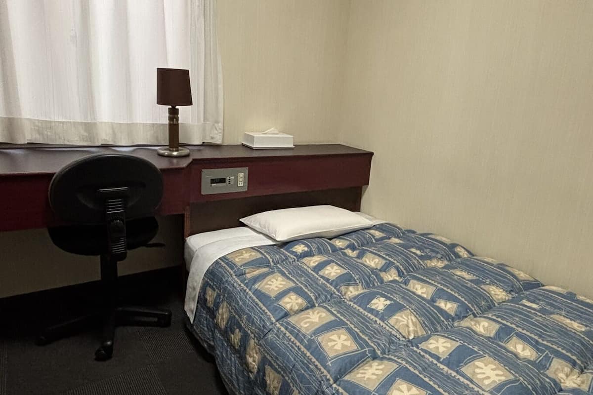 Una habitación de hotel con una cama, un escritorio, una silla, una lámpara y un ventanal con cortinas.