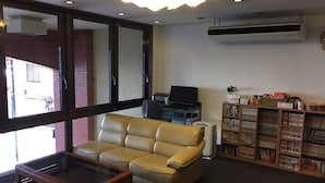 A living room with a leather sofa, a glass-top coffee table, a television on a stand, and a bookshelf filled with books. - Hotel Town Nishikigawa (Kochi)