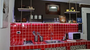 A kitchen with red tiles, a microwave, a sink, and hanging shelves with kitchenware. - Guest House La Casetta (Piazza Armerina)