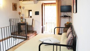 A bedroom with a bed, a TV, a window with curtains, a staircase, and a small table with flowers. - Guest House La Casetta (Piazza Armerina)