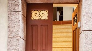 A brown door with a decorative glass panel and a mail slot, leading to a staircase with a stone wall on either side. - Guest House La Casetta (Piazza Armerina)