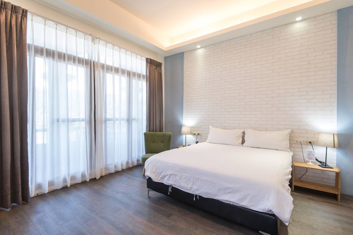 Ett modernt hotellrum med en stor säng, en grön fåtölj och en vägg med ett mönster som efterliknar tegelstenar.