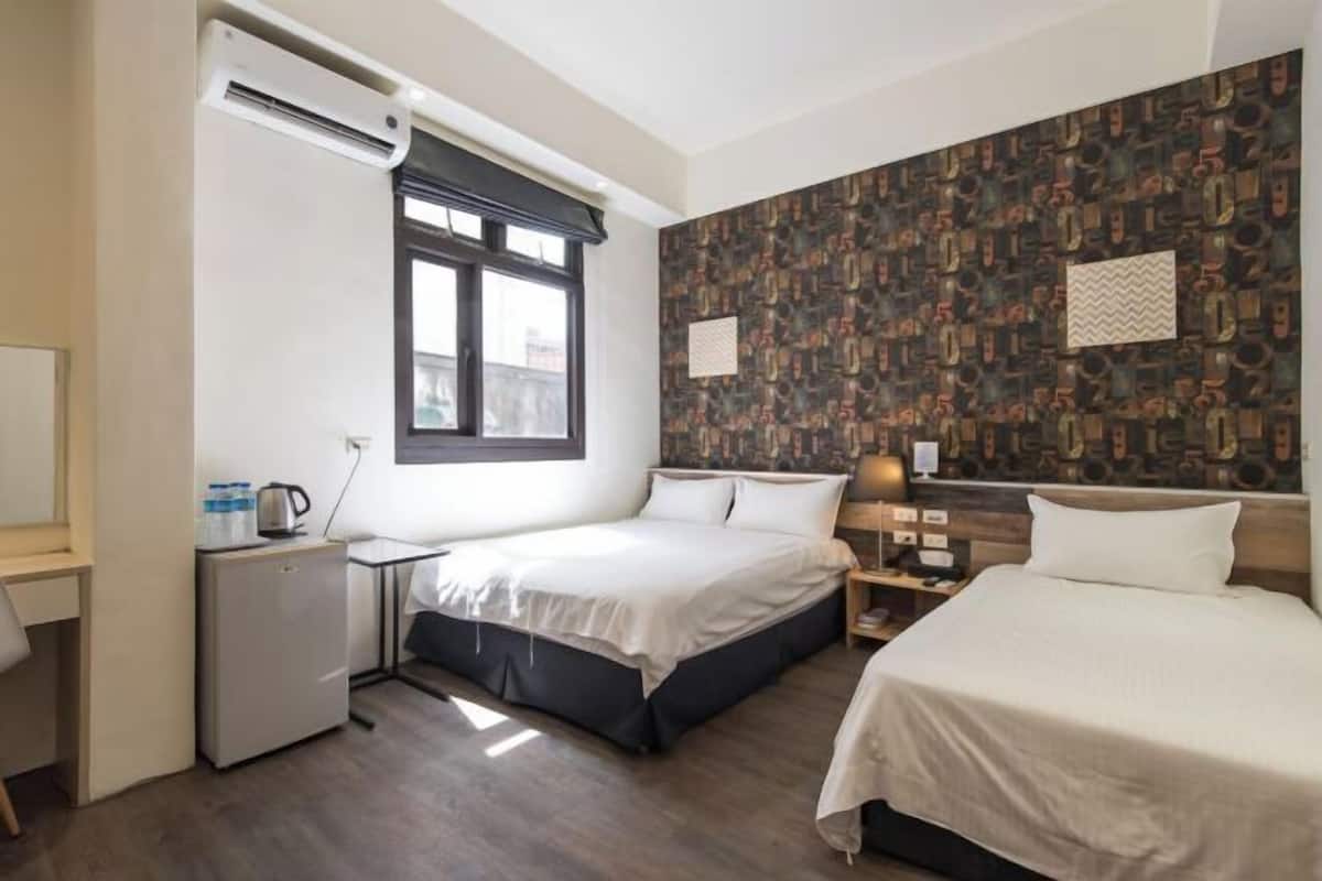 Ett hotellrum med två sängar, ett skrivbord med en dator, ett litet kylskåp och ett fönster med persienner.