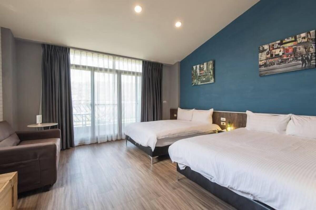 Ett hotellrum med två sängar, en soffa, ett litet bord och ett stort fönster med gardiner.