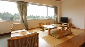 A room with tatami mats, a low table, chairs, a television, and a view of trees through a window. - Kagetsuen (Hakone)