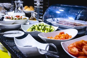 A buffet with various food items including sliced cucumbers, tomatoes, and olives.