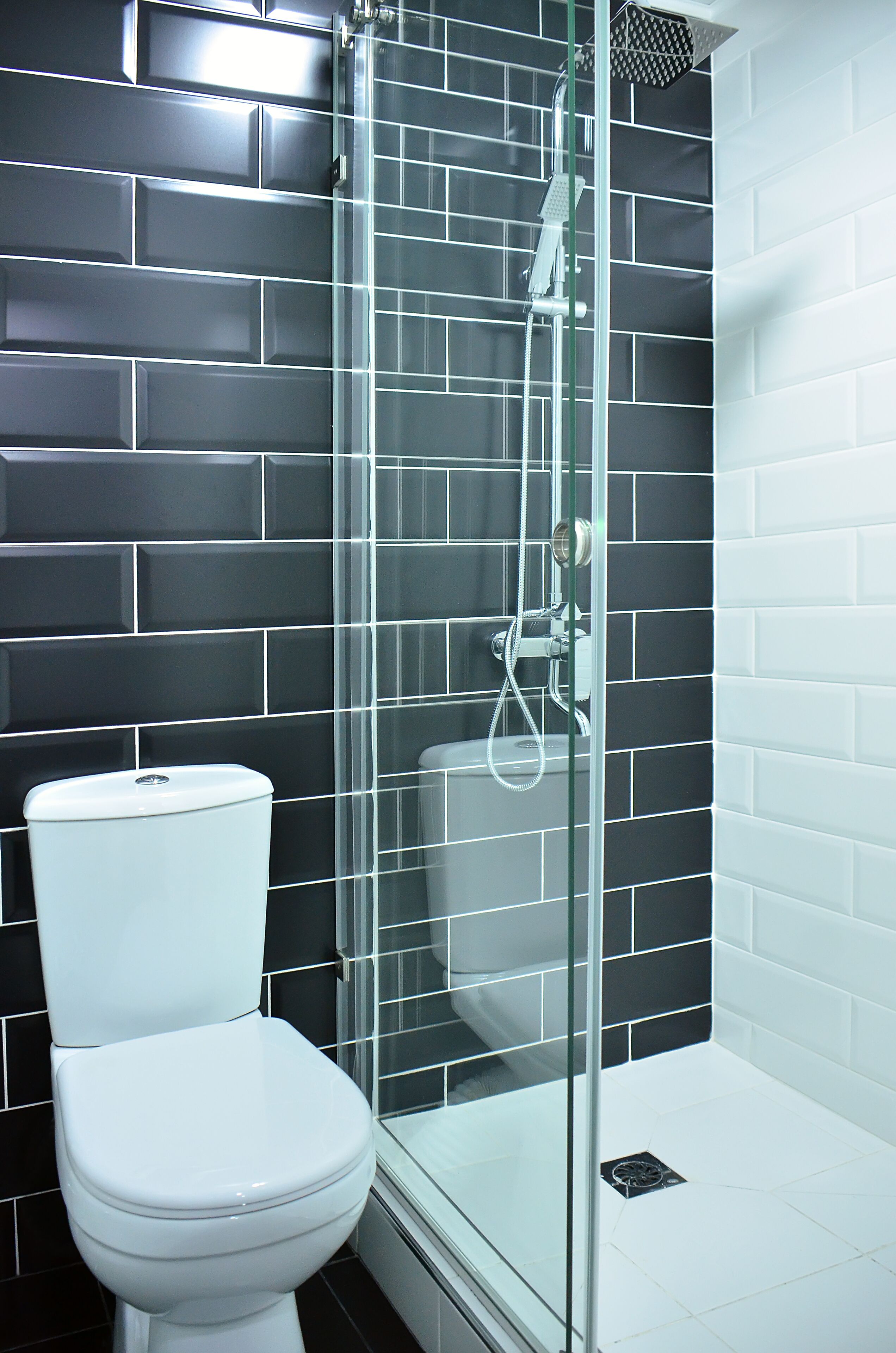 A modern bathroom with a glass-enclosed shower, a white toilet, and black tiled walls.