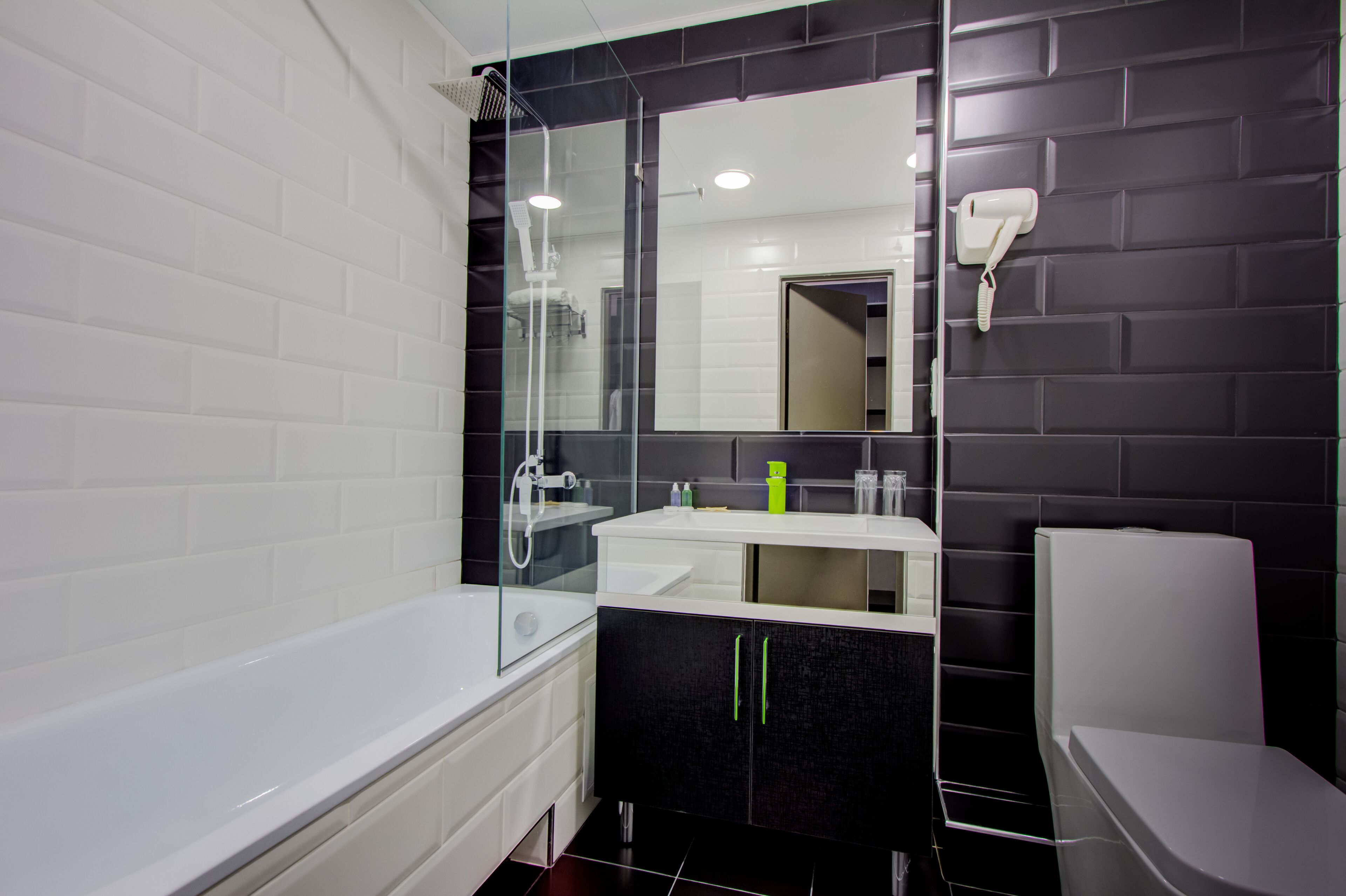 A modern bathroom with a white bathtub, a glass-enclosed shower, a black and white vanity, and a white toilet.