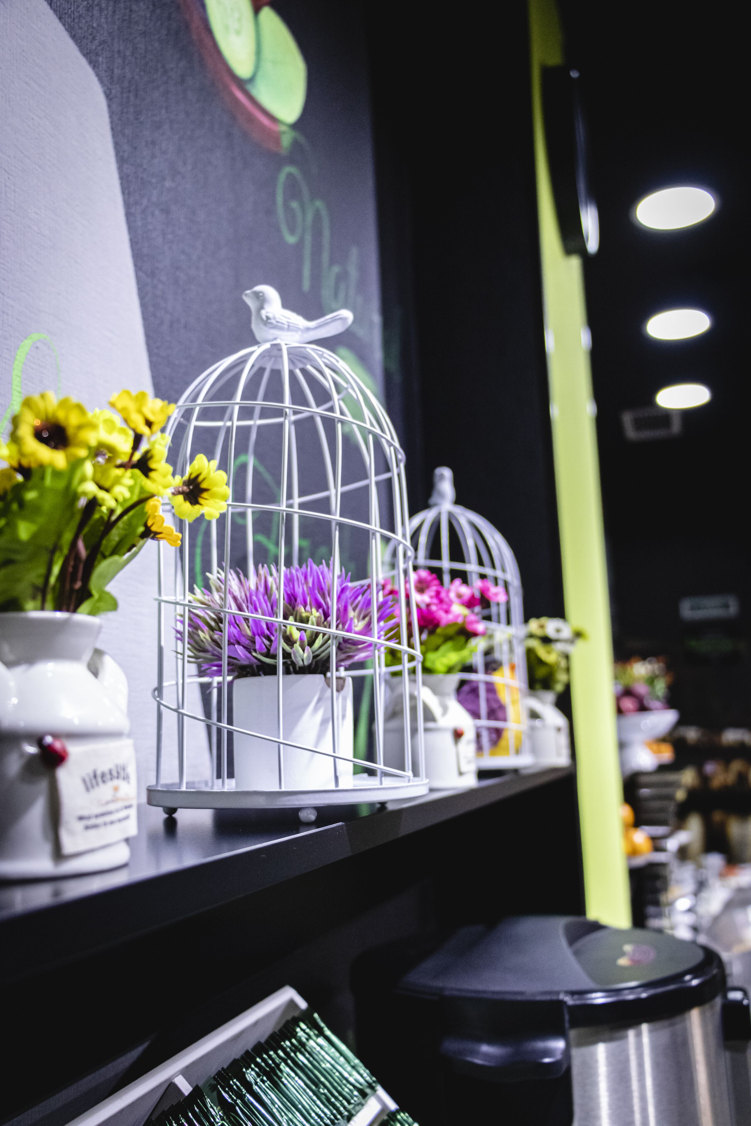 A bar area with a counter, a coffee machine, and decorative birdcages with flowers.
