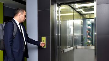 Un home amb armari pressiona un botó del panell de control d'un ascensor en un edifici modern.