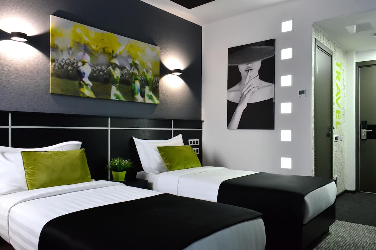 Een moderne hotelkamer met twee bedden, een groot abstract schilderij, een portret en een 'TRAVEL' bord aan de muur.