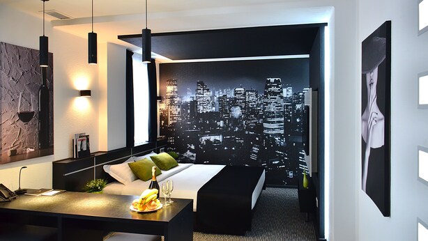 Ein modernes Hotelzimmer mit Stadtbild-Wandgemälde, einem Schreibtisch mit Laptop und einem Bett mit Kissen.