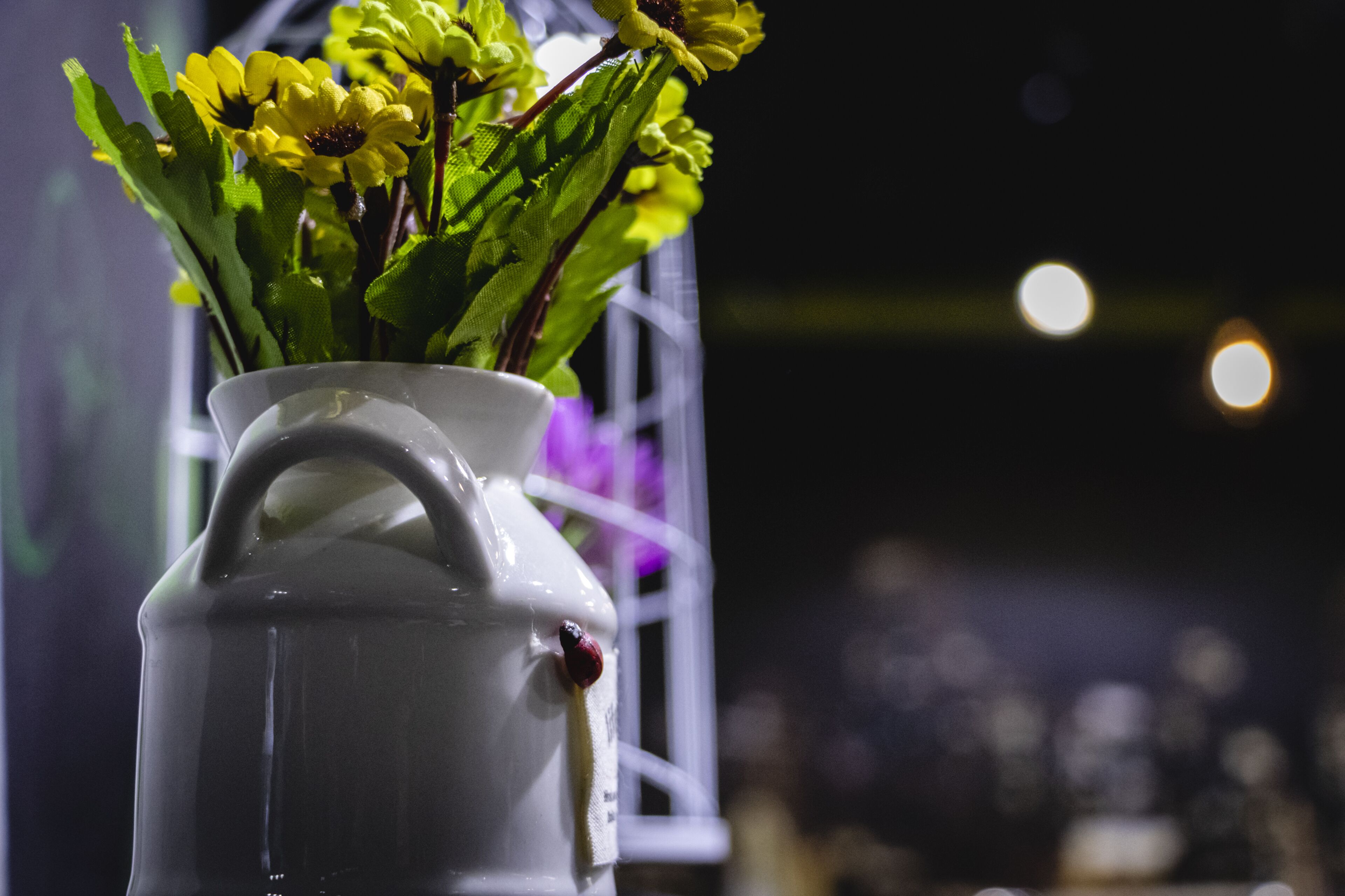 A white ceramic vase with a handle containing yellow flowers and green leaves.