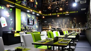 Ein Restaurant mit grünen und weißen Stühlen, schwarzen Tischen und Blick auf die Stadt.