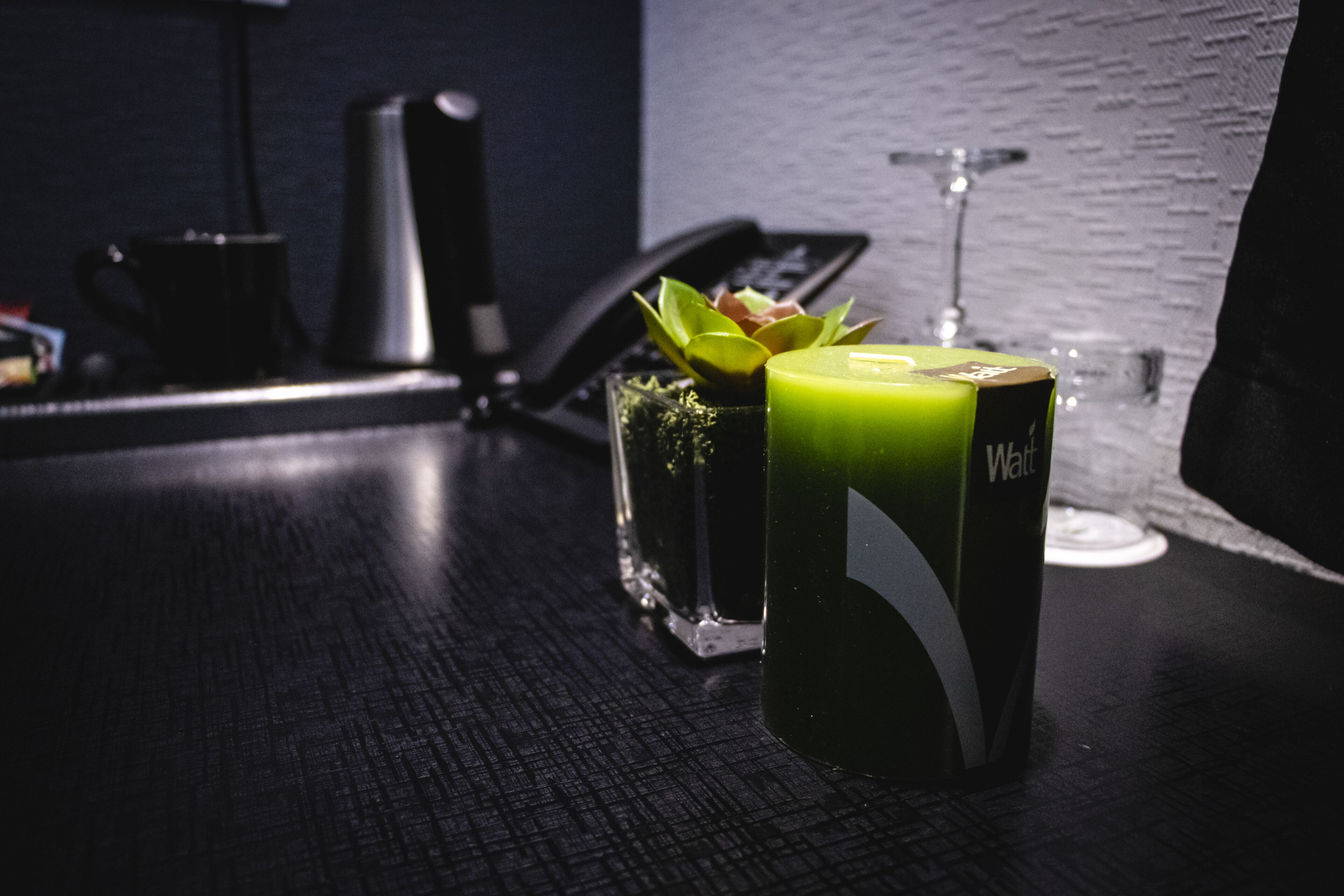 A desk with a green drink, a glass with a plant, and a black telephone.