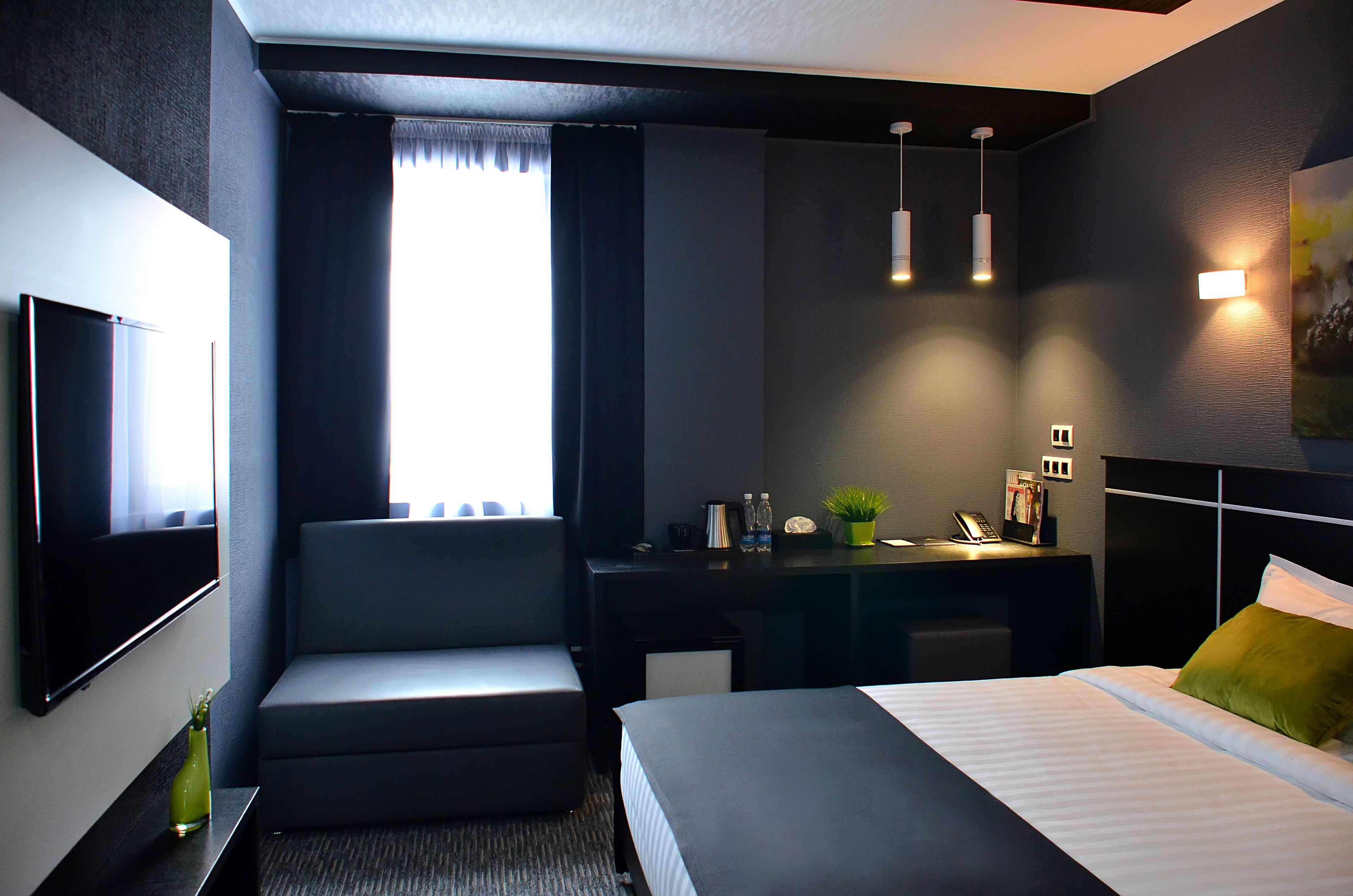 A modern hotel room with a bed, a desk, a chair, a TV, and a window with curtains.
