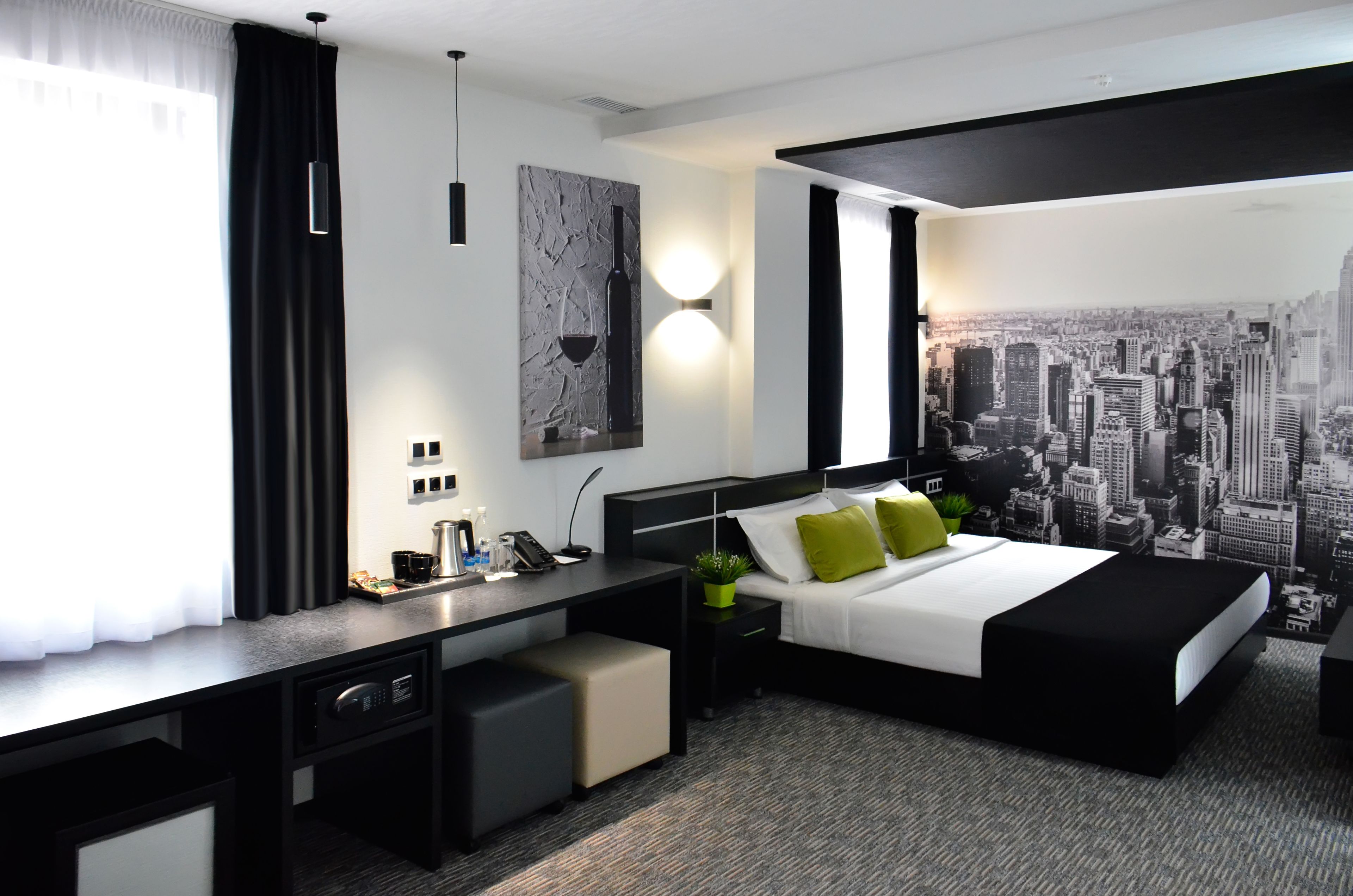 A modern hotel room with a bed, desk, and cityscape wallpaper.