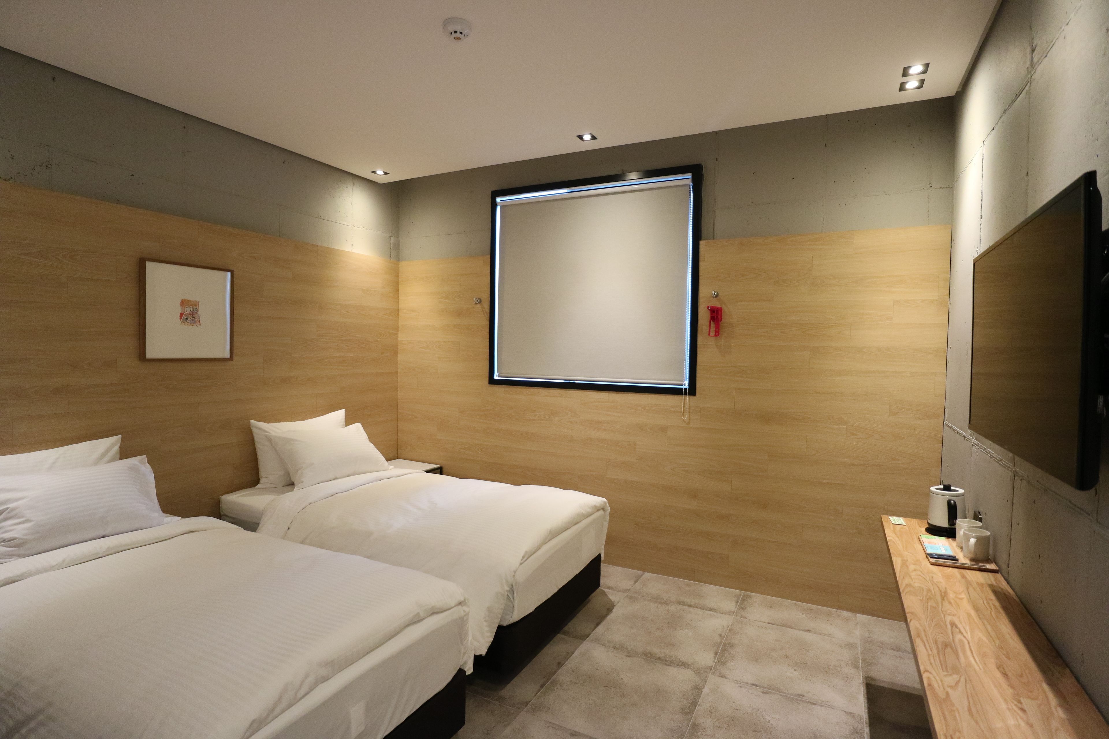 Una habitación de hotel moderna con dos camas, un panel de pared de madera, un espejo grande y una pequeña mesa con hervidor y tazas.