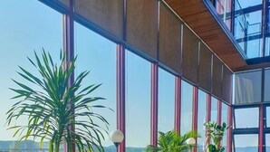 A modern dining area with large windows, wooden tables, and chairs, featuring a view of greenery and distant buildings. - The HongC Hotel Gangneung (Gangneung)