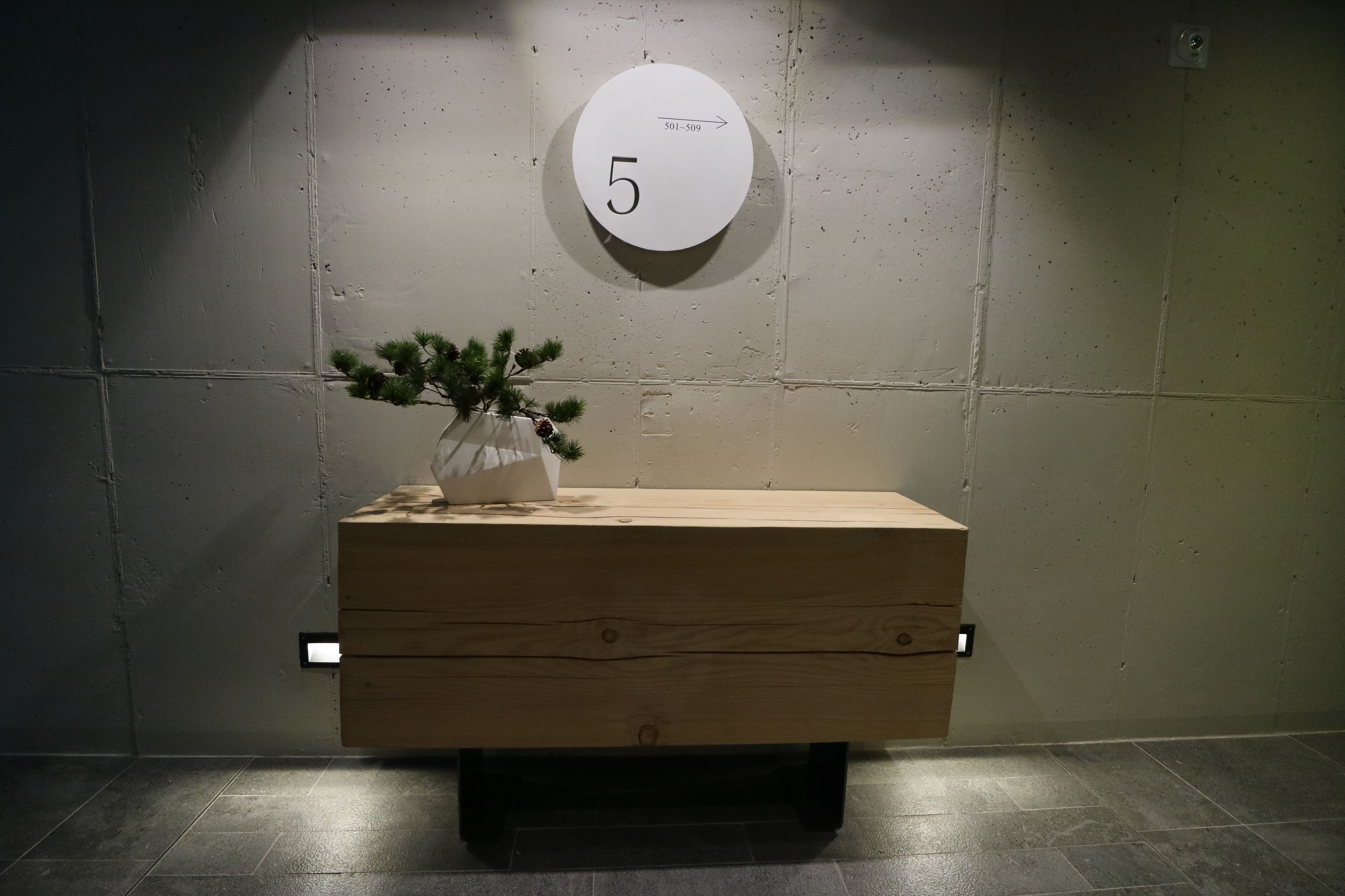 A wooden bench with a potted plant, a wall-mounted number sign, and a light switch.