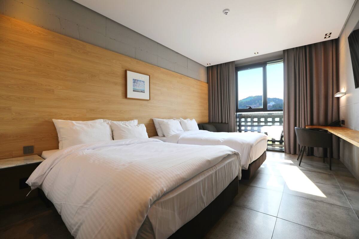 Une chambre d’hôtel avec deux lits, un bureau et une vue sur l’extérieur.